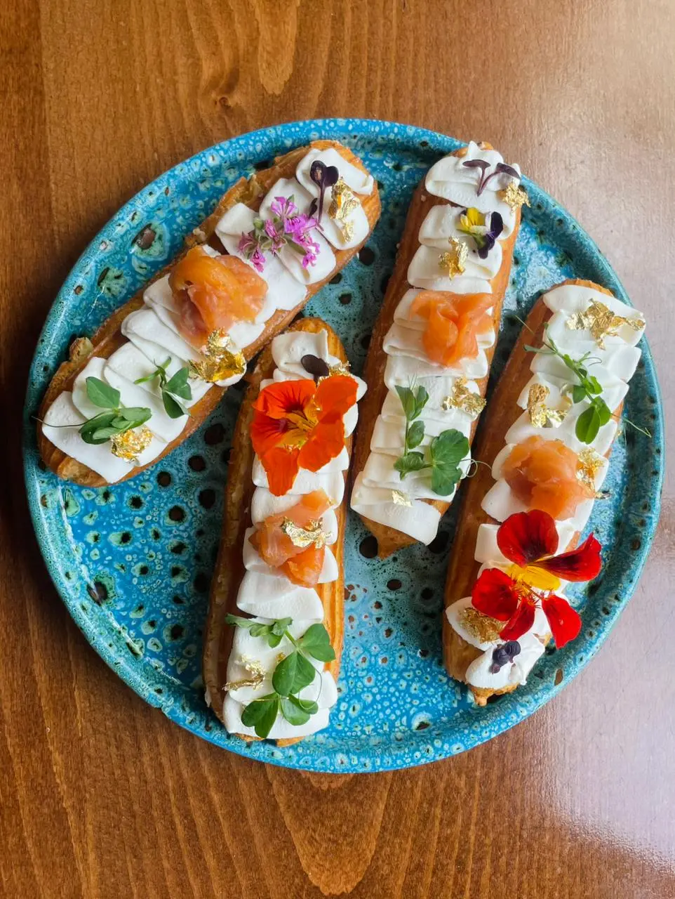 Éclairs à la crème et au saumon fumé, dressés à la main avec fleurs comestibles et feuille d'or.